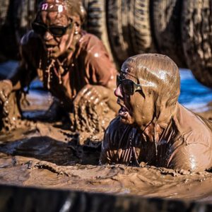 Zwei schlammige Frauen, die aus einem schmutzigen Bad auftauchen und Luft schnappen - Muddy Angel Run 2022