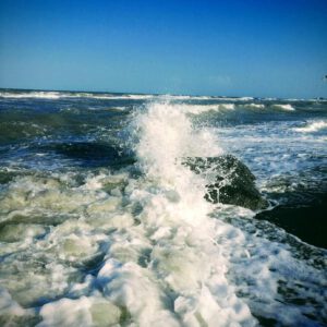 Gischt bricht sich an einem Findling am Ostseestrand